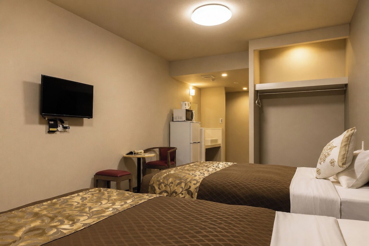 A hotel room with two beds, a TV, a desk with a chair, and a wardrobe.