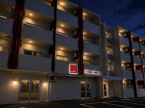 A multi-story hotel with a modern design, featuring balconies on each floor and a prominent signage. - Mr.KINJO Happiness Resort 1 (Miyakojima)