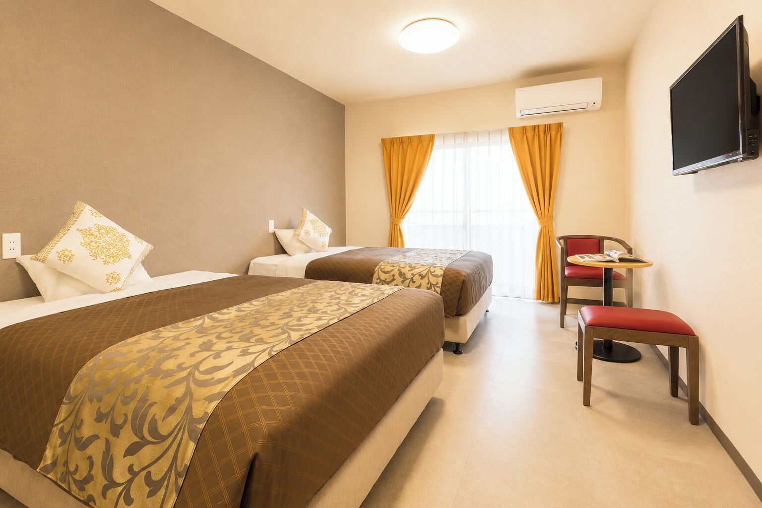 Habitación de hotel con dos camas, televisión, aire acondicionado, una mesita con una silla y una ventana con cortinas.