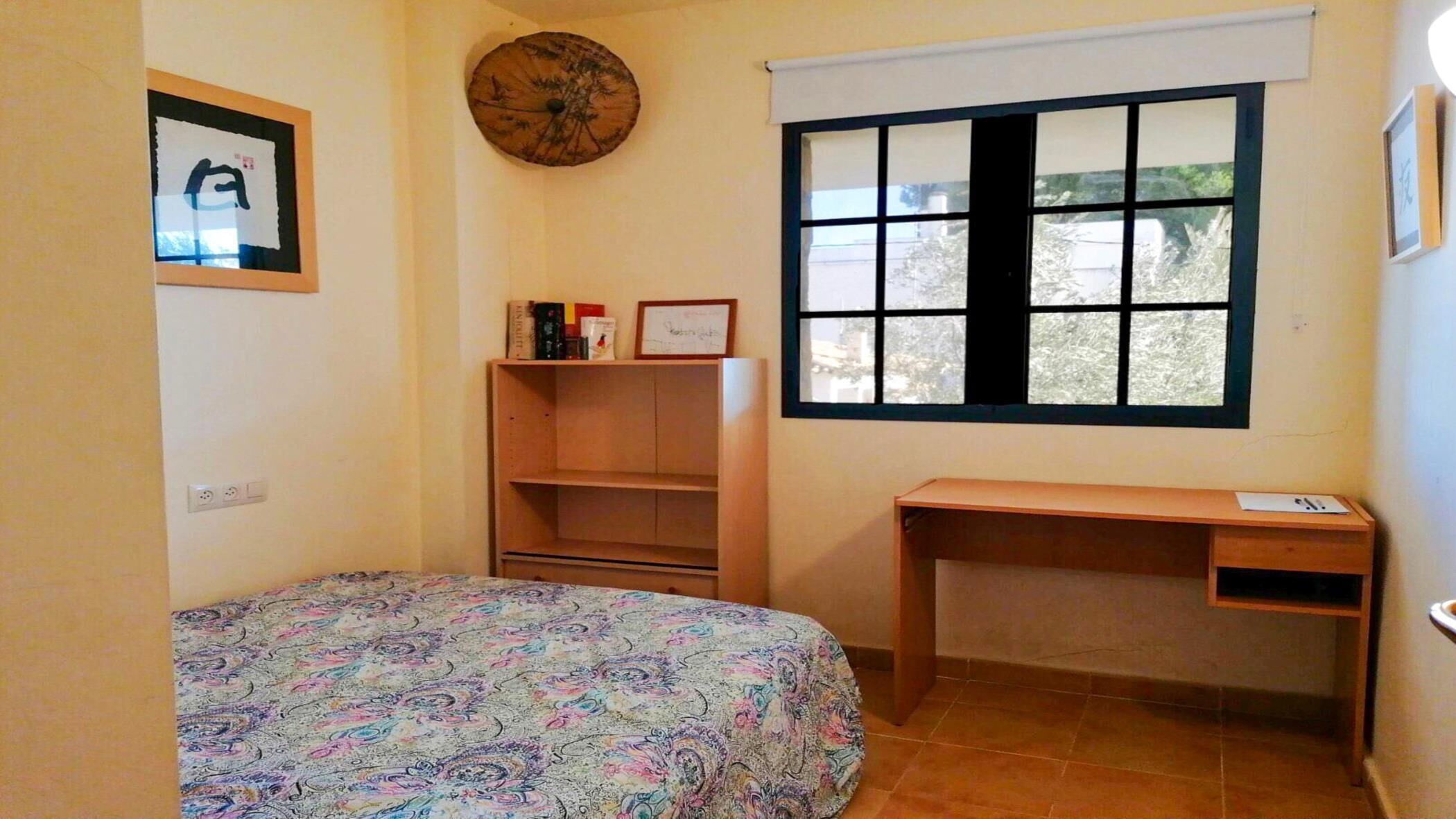 A small, tidy bedroom with a bed, a desk, and a window.