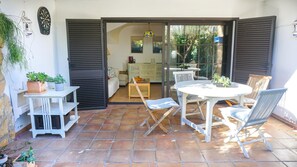 A patio with a table and chairs, a potted plant, and a sliding glass door leading to an interior space with a bed and a cabinet. - VACAY L'Escala – Gala Duplex with Pool and Parking near Riells Beach (l'Escala)
