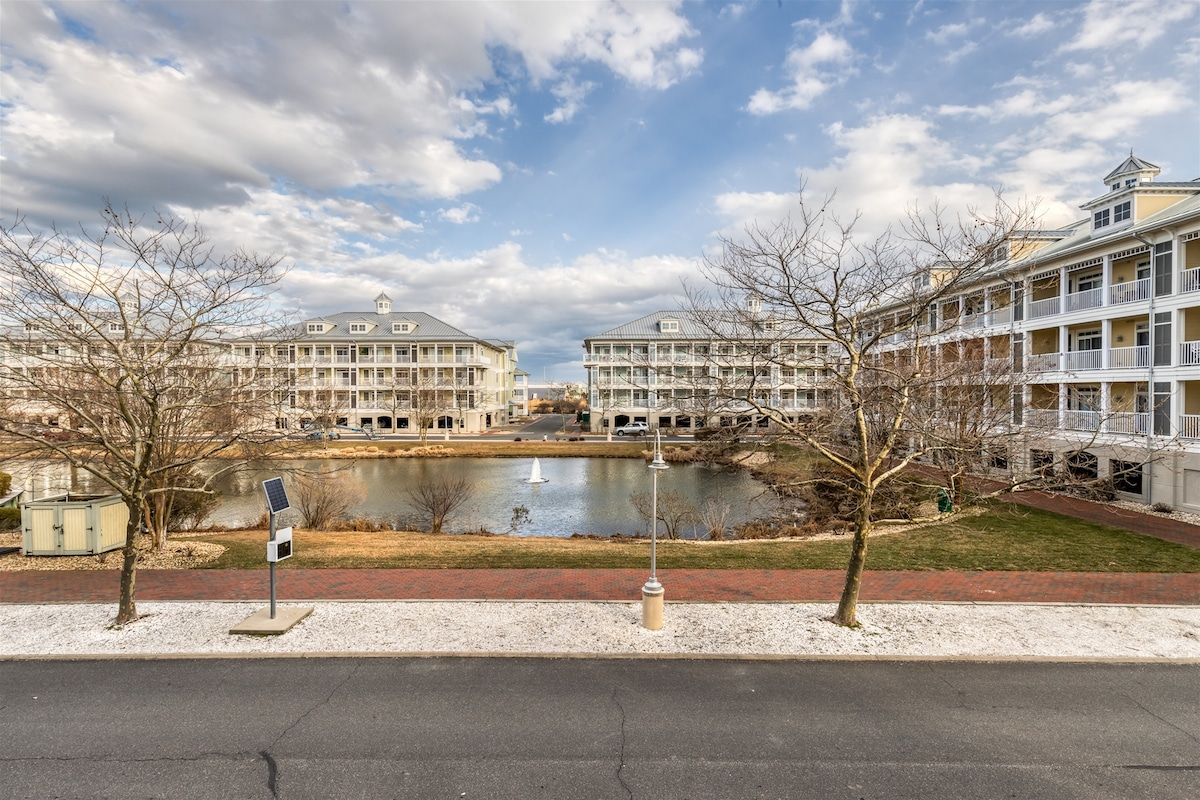 A waterfront hotel with multiple balconies, a pond, and a pedestrian path.