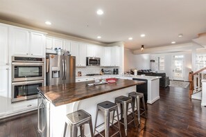 Een moderne keuken met witte kasten, roestvrijstalen apparatuur, een houten kookeiland met barstoelen en een donkere houten vloer.