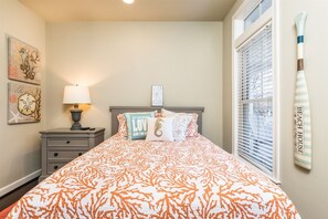 Un dormitorio con cama, mesita de noche, lámpara y ventana con persianas.
