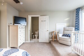 A bedroom with a television on a dresser, a crib with a patterned pillow, and a door leading to a bathroom. - Sunset Island 13 Fountain Drive West (Ocean City)
