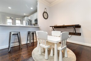 A dining area with a white table and chairs, a clock on the wall, and a wooden shelf with glasses. - Sunset Island 13 Fountain Drive West (Ocean City)