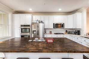 Cocina con armarios blancos, electrodomésticos de acero inoxidable y una isla de madera oscura.