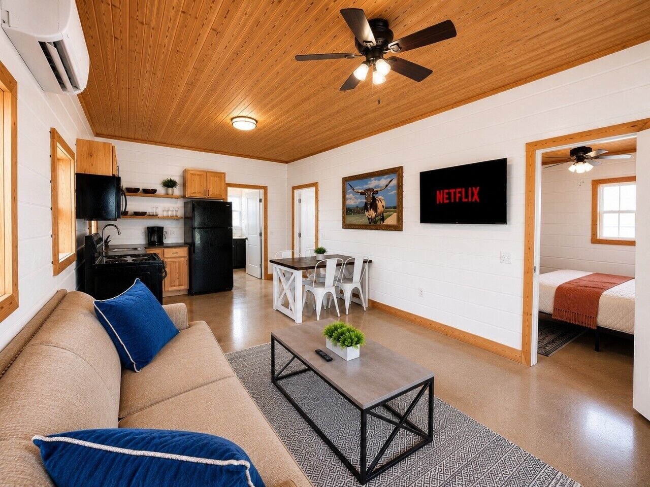A modern living space with a sofa, coffee table, dining table, chairs, kitchen area, and a TV mounted on the wall.