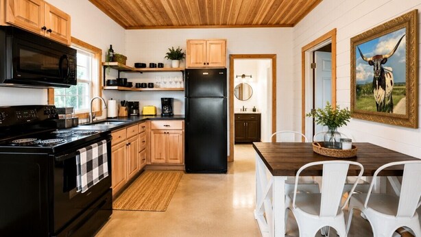 Eine Küche mit Holzausstattung, einem schwarzen Kühlschrank und einem Essbereich mit weißen Stühlen.