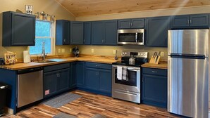 A modern kitchen with dark blue cabinets, stainless steel appliances, and a wooden ceiling. - Mtn Rd Cottage -HOT TUB-Close 2 Camelback/Shopping (Tannersville)