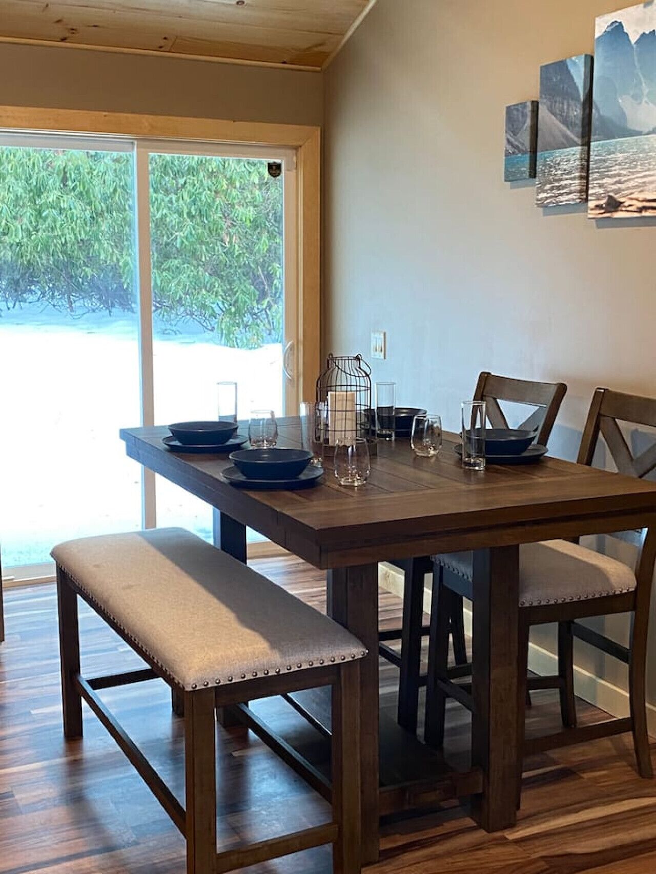 A dining area with a wooden table set for four, benches, and a view of greenery outside.