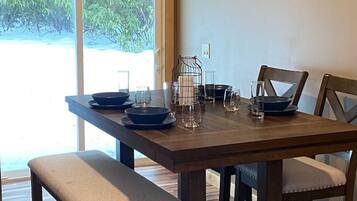 A dining area with a wooden table set for four, benches, and a view of greenery outside.