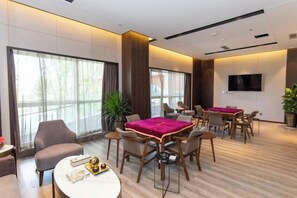 Habitación de hotel moderna con zona de comedor, ventanas amplias y televisión de pantalla plana.