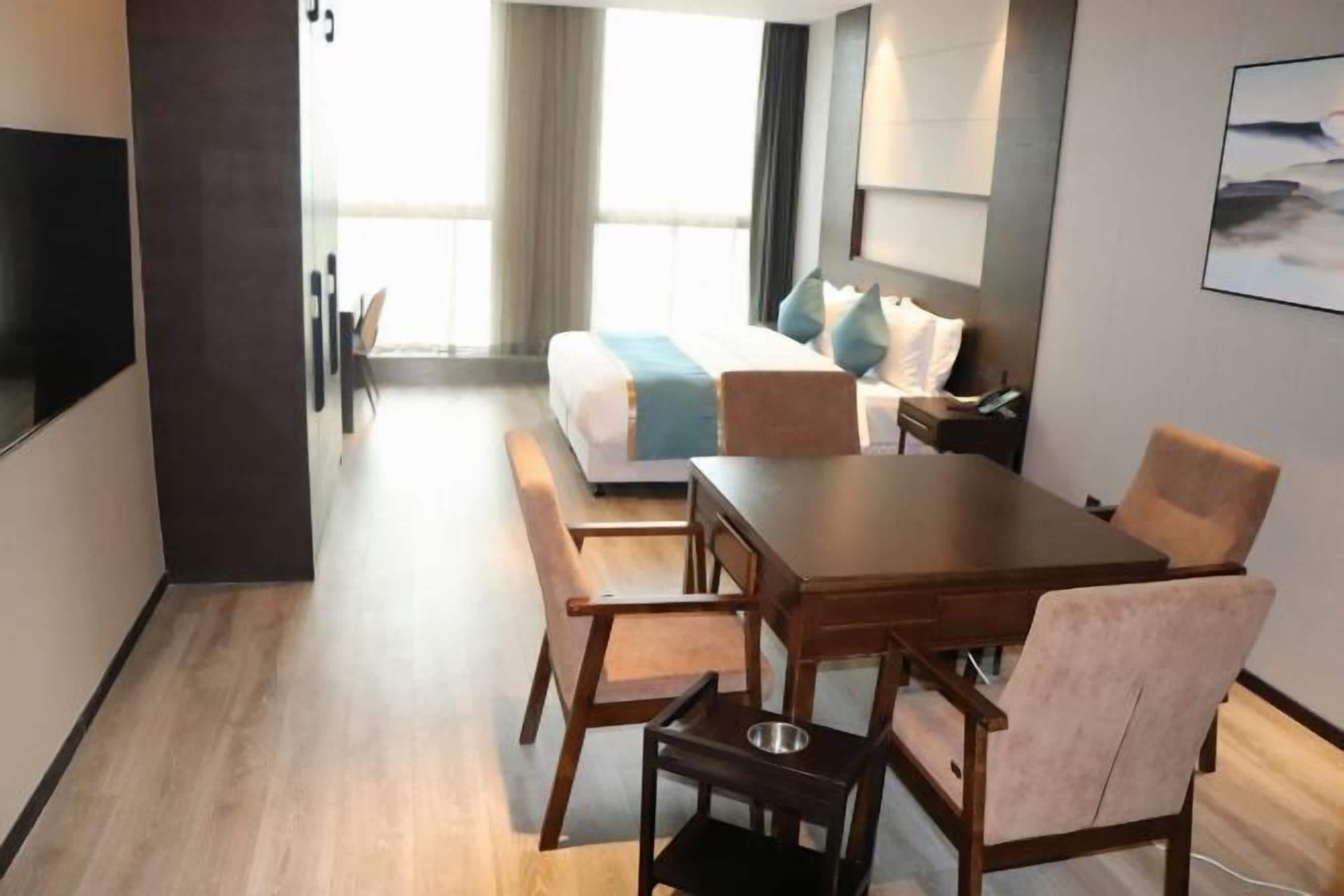 A hotel room with a bed, a desk, and a chair. There is a window with curtains, and a painting on the wall.