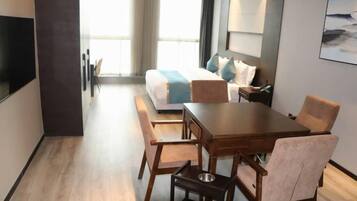 A hotel room with a bed, a desk, and a chair. There is a window with curtains, and a painting on the wall.