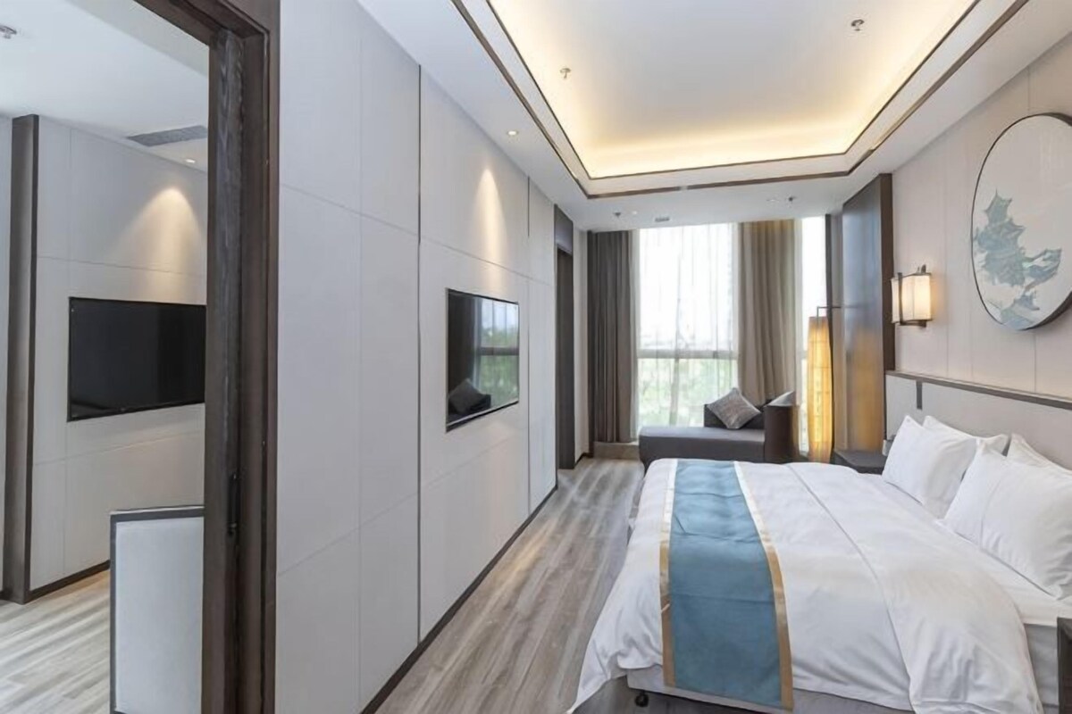 Una habitación de hotel moderna con una cama grande, un televisor de pantalla plana, un área de descanso y un ventanal amplio.