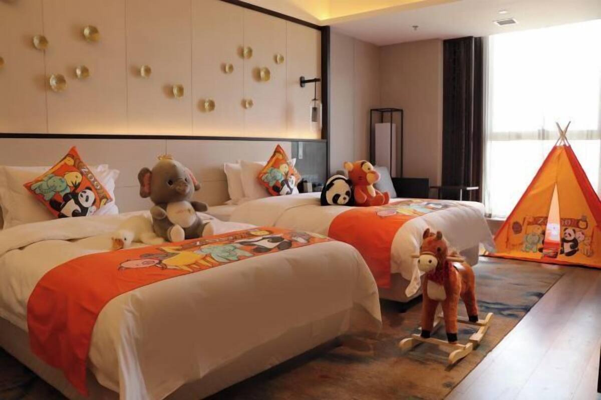 Habitació d'hotel amb dos llits, joguines de peluix, un tipi i una finestra gran.