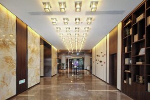 Un pasillo de hotel con piso pulido, techo con iluminación empotrada y una estantería a la derecha.