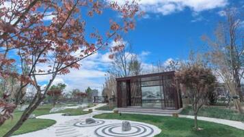 A modern building with a glass facade, surrounded by a landscaped garden with circular stone patterns and trees.