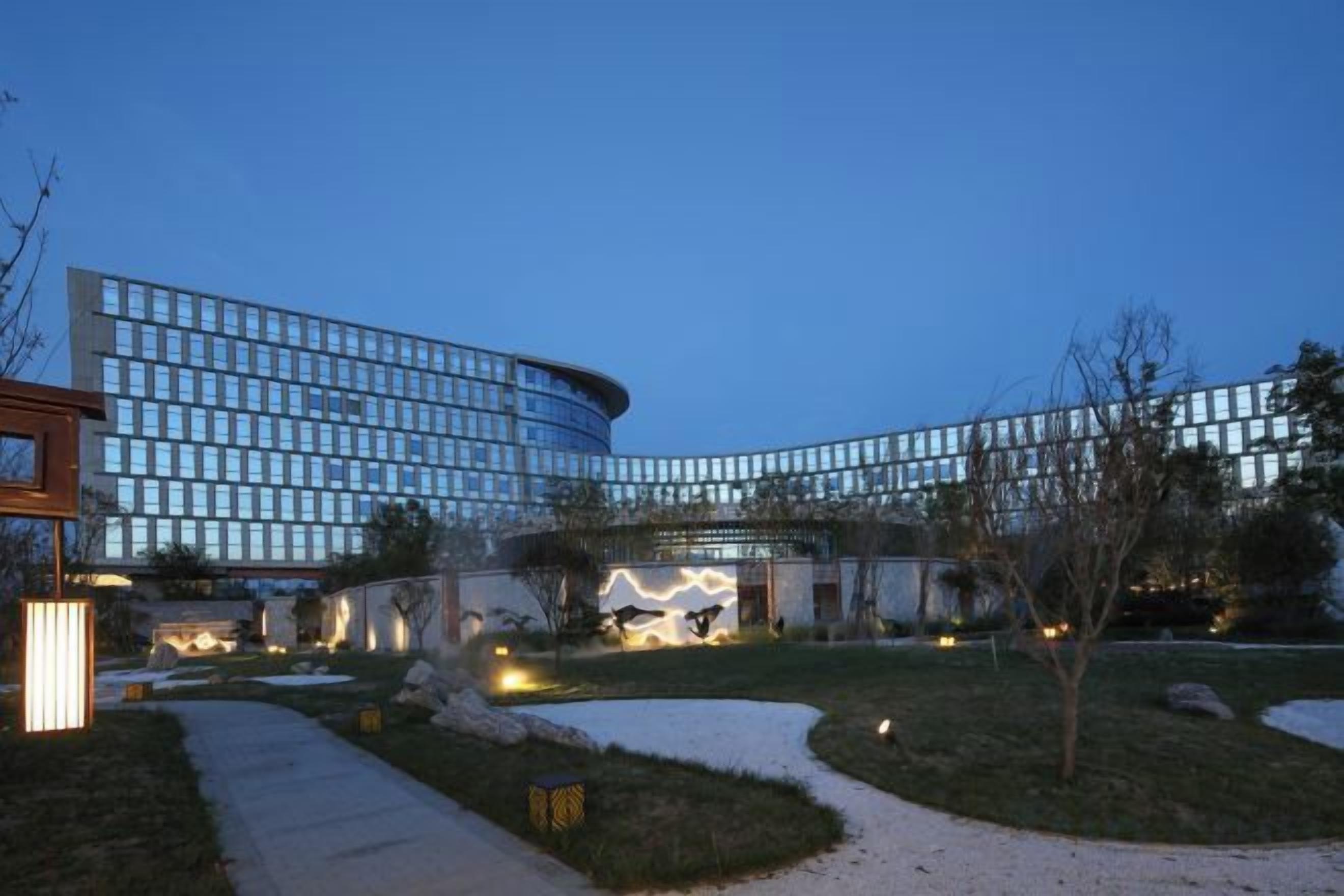 A modern building with a curved facade, a landscaped courtyard, and a pathway leading to the entrance.
