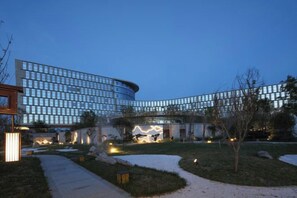 A modern building with a curved facade, a landscaped courtyard, and a pathway leading to the entrance.