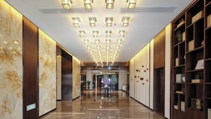Un moderno vestíbulo de hotel con piso de mármol pulido, una lámpara central y estanterías de madera con objetos decorativos.