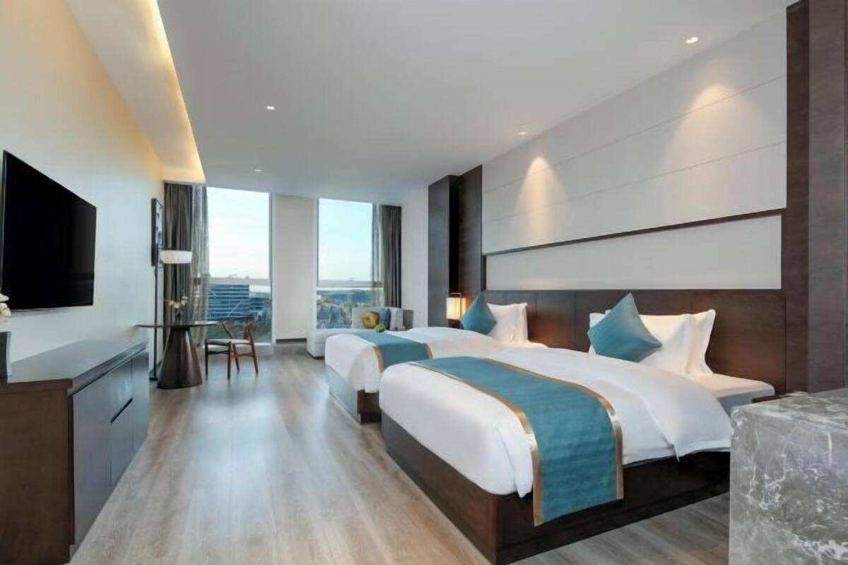Habitació d'hotel moderna amb dos llits, un escriptori i un gran finestral que ofereix vista a la ciutat.