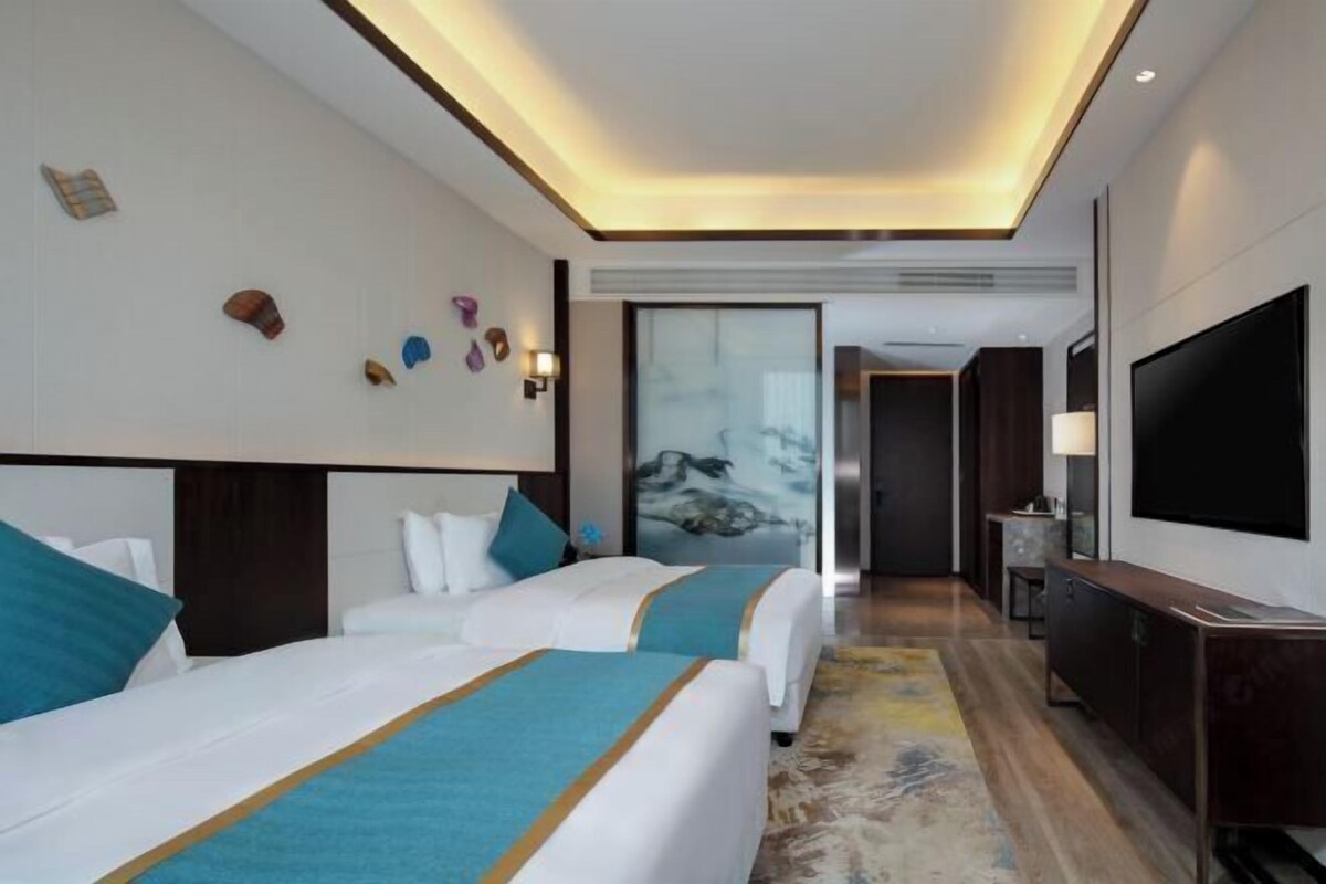 Habitación de hotel con dos camas, televisión, escritorio y un cuadro en la pared.