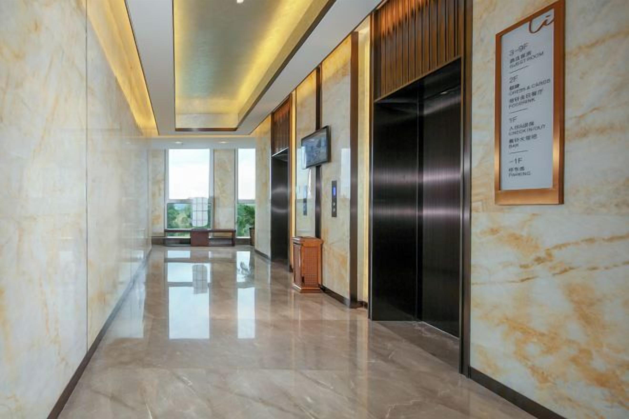 A hotel lobby with a marble floor, an elevator, and a television mounted on the wall.