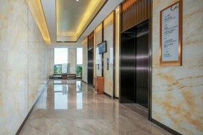 Un vestíbulo de hotel con piso de mármol, un ascensor y un televisor montado en la pared.