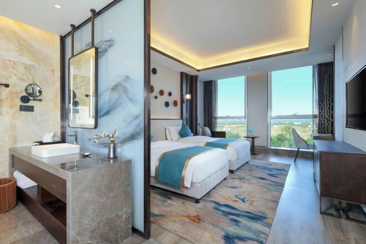 Una habitación de hotel moderna con una cama grande, un escritorio, un baño con tocador de mármol y un ventanal con vistas al paisaje.