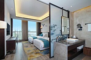 Una habitación de hotel moderna con una cama grande, un escritorio, un baño con tocador y vistas a la ciudad.