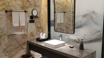 A modern bathroom with a marble wall, a large mirror, a white sink, and a towel rack.