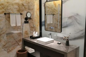 Un baño moderno con pared de mármol, un espejo grande, un lavamanos blanco y un perchero para toallas.