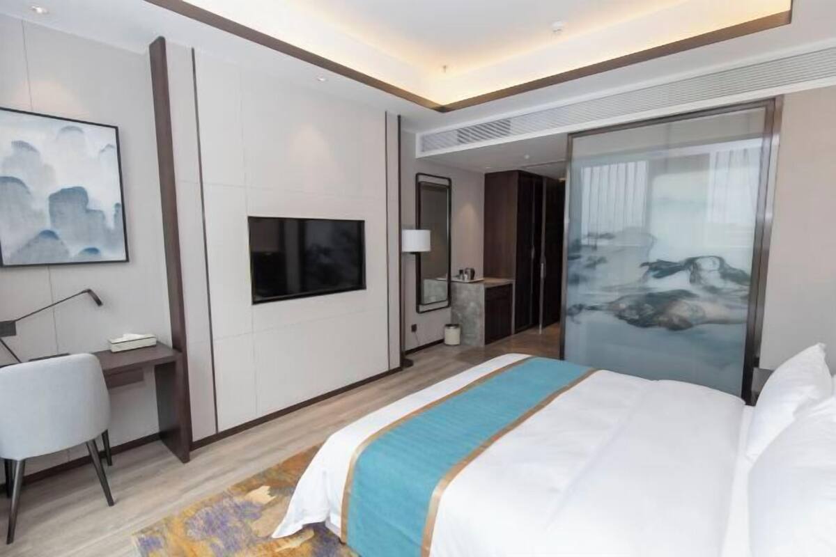 Habitació d'hotel moderna amb un llit gran, una escriptori, una televisió i una porta corredissa que dona a un bany.
