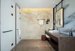 Un baño moderno con pared de mármol, un espejo grande, un lavamanos y un perchero para toallas.