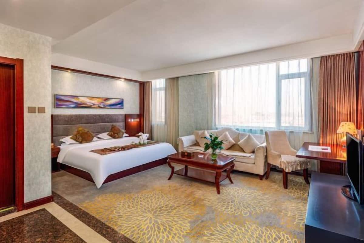Quarto de hotel com cama, sofá, mesa de centro, televisão e um quadro na parede.