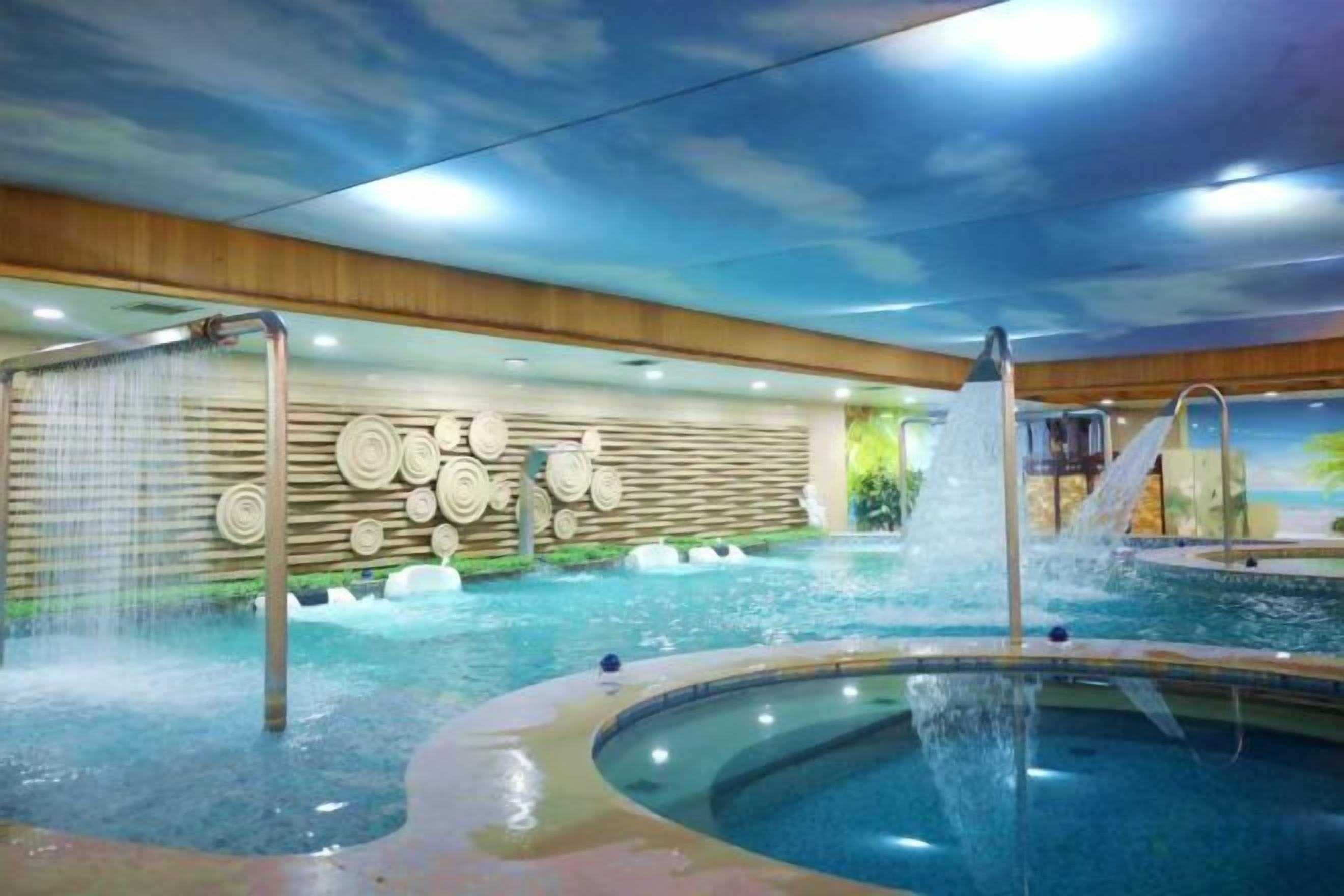 An indoor swimming pool with a water fountain, a wall with circular patterns, and a ceiling with a cloud design.