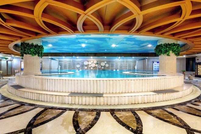 Une piscine circulaire dotée d’un espace central aménagé en salon, entourée d’une plateforme à plusieurs niveaux.