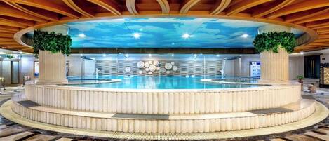 Une piscine circulaire dotée d’un espace central aménagé en salon, entourée d’une plateforme à plusieurs niveaux.
