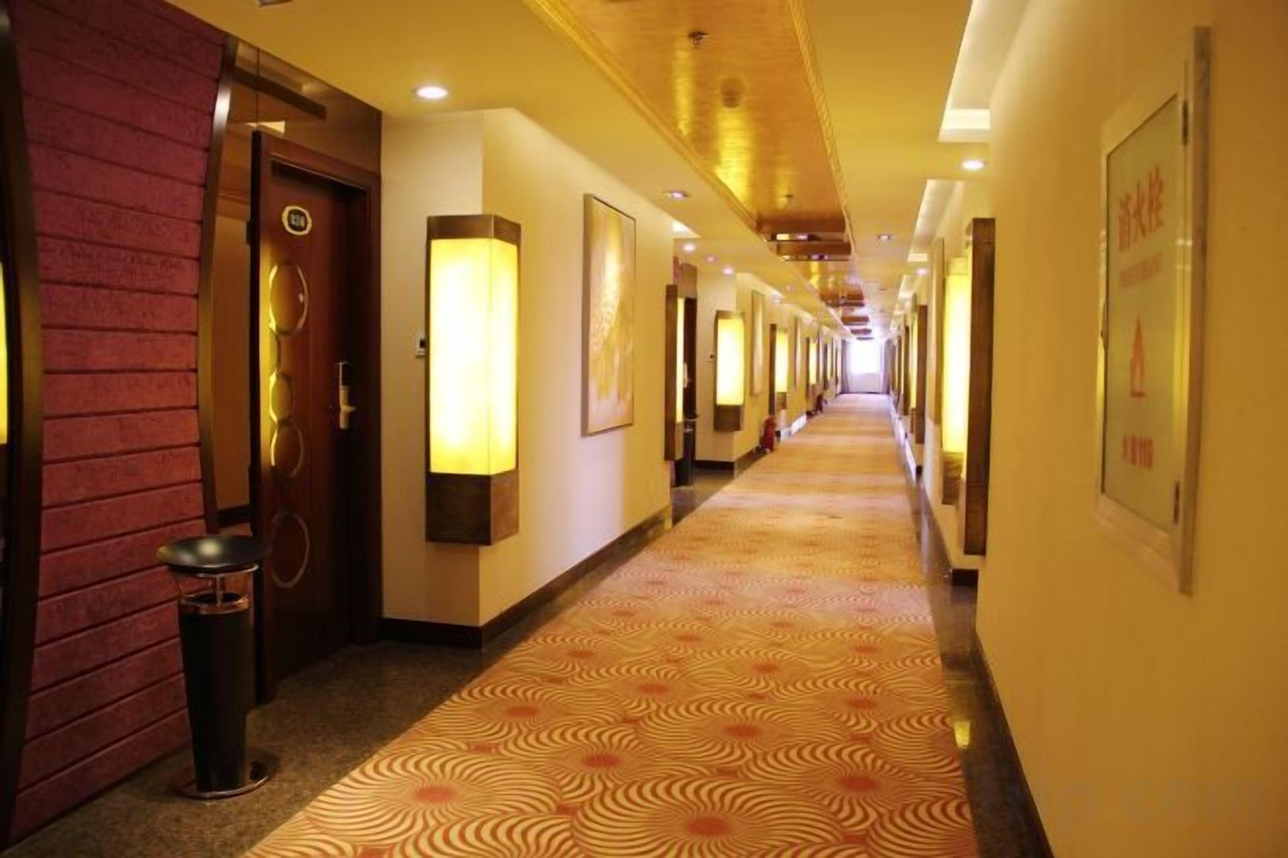 A hotel corridor with doors, wall-mounted lights, and a patterned carpet.