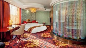 Habitación de hotel con cama curva, escritorio, silla y ventana grande con cortinas.