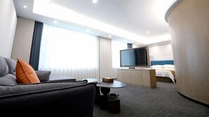 Una habitación de hotel moderna con sofá, televisión, cama y pared curva.