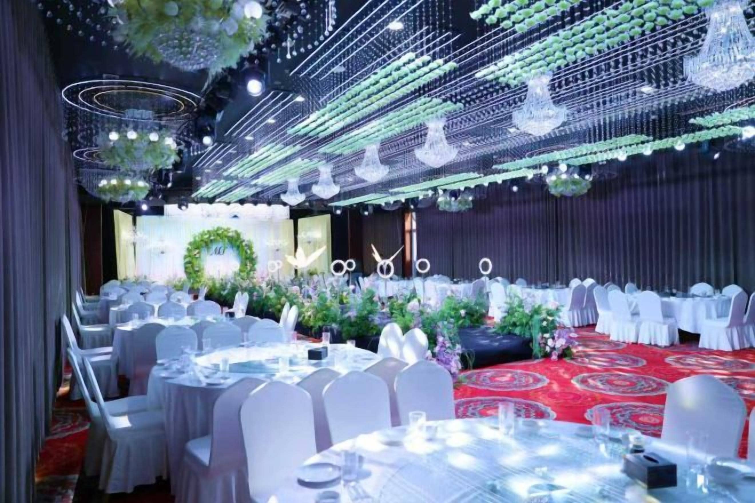 A banquet hall with round tables, white chairs, and a red carpet.