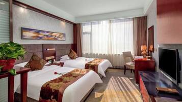Habitación de hotel con dos camas, televisión, escritorio, silla y ventana grande con cortinas.
