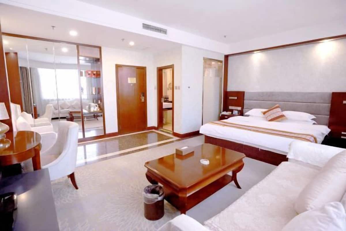 Quarto de hotel com cama, sofá, mesa de centro, escrivaninha e espelho.