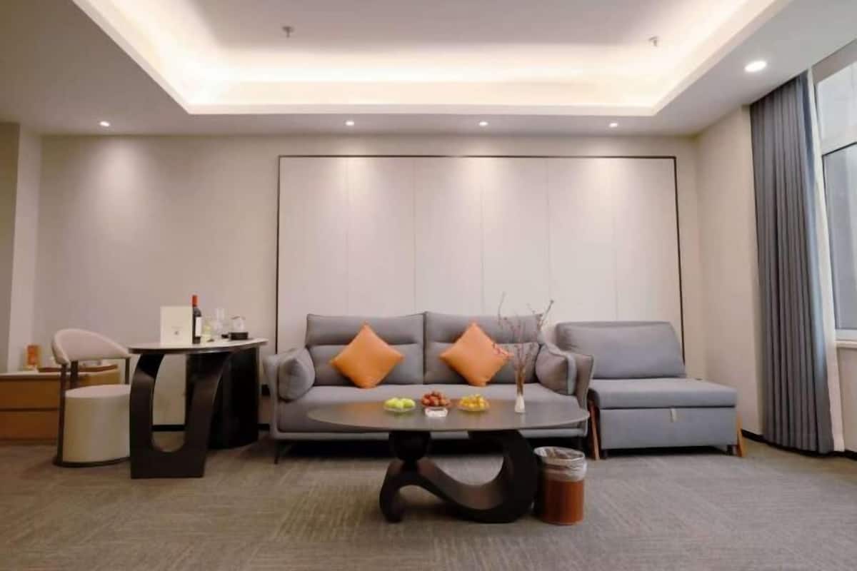 Uma sala de estar moderna com um sofá cinzento, duas almofadas laranja, uma mesa de centro redonda e uma mesa lateral com uma garrafa.