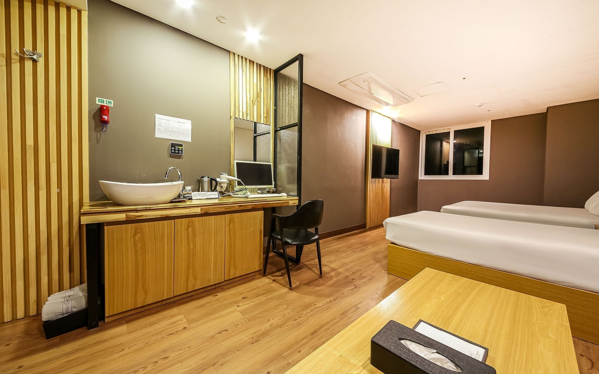 A hotel room with a wooden desk, a large mirror, a sink, a bed, and a television.