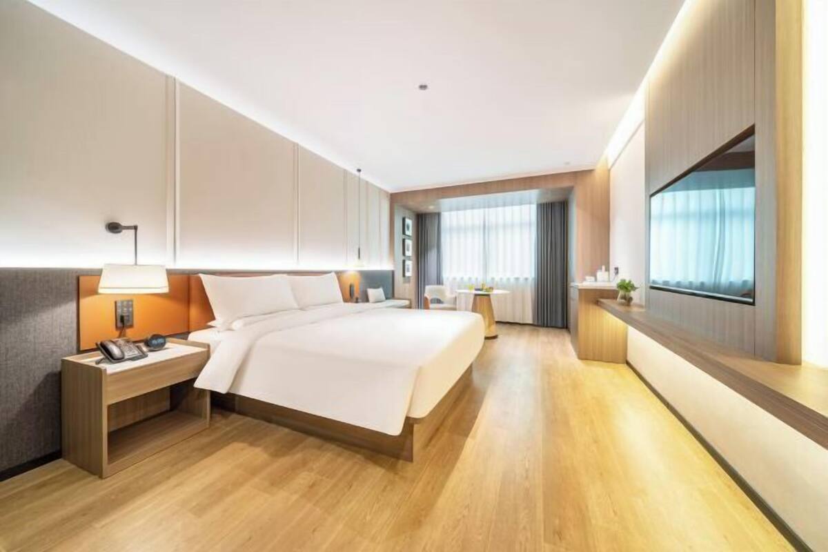 A hotel room with a bed, bedside table, lamp, and a TV on the wall.
