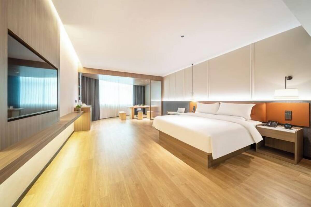 A modern hotel room with a large bed, bedside tables, a TV, and a view of the city.